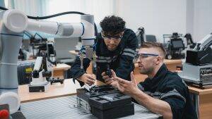 Student engineer Assembling Robotic Arm with computer in Technology Workshop. Service Engineer Holding Robot Controller and Checking Robotic Arm Welding Hardware.